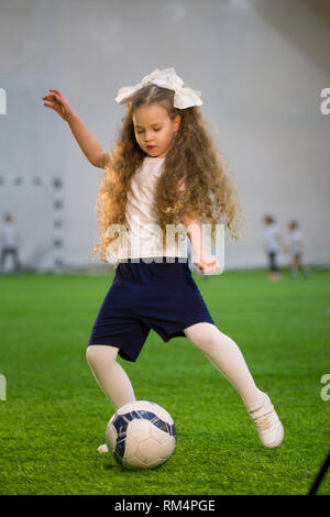 Una ragazzina di calciare la palla sul campo di calcio Foto Stock