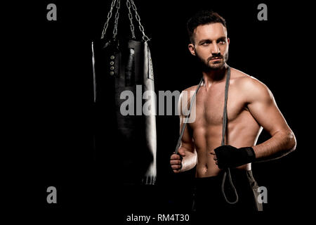 Bello il boxer in piedi con salto con la corda nei pressi di sacco da boxe isolato su nero Foto Stock