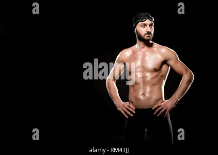 Nuotatore muscolare in piedi in cuffia per la piscina e nuotare gli occhiali di protezione isolati su nero Foto Stock