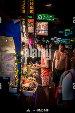 Turista che acquista cibo di strada da una bancarella in un mercato a Phuket, Thailandia. Foto Stock