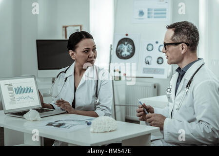 Dai capelli scuri medico femmina con uno stetoscopio sul suo collo sostenendo Foto Stock