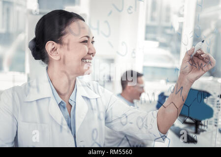 Felice scienziato romanzo scrittura di formule chimiche sul bordo del vetro Foto Stock