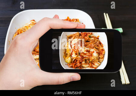 Concetto di viaggio - visitatore fotografie di cucina coreana di kimchi (antipasto piccante cavolo nappa) nella ciotola bianco sullo smartphone Foto Stock