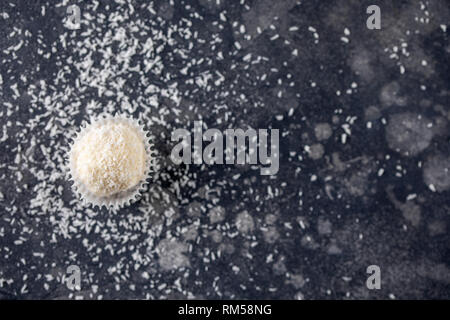 Candy tartufi snowball su sfondo scuro con spazio per il testo. Bianco Noce di cocco dolci tartufi su uno sfondo scuro. Foto Stock