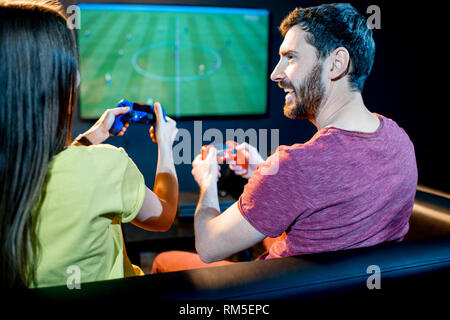 Giovani entusiasti matura la riproduzione del gioco del calcio con console di gioco seduti sul divano a giocare club Foto Stock