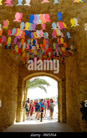 Trippers giorno e turisti a piedi attraverso la addobba portone che conduce nella strada principale su isola di Tabarca, Alicante, Spagna Foto Stock