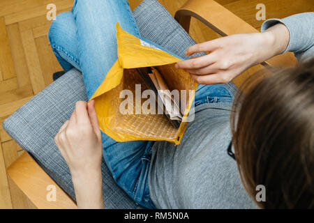 Parigi, Francia - Novembre 4, 2017: curioso donna unboxing sul soggiorno poltrona la perfezione del Amazon busta scatola di cartone con più note di carta interno e un regalo Foto Stock