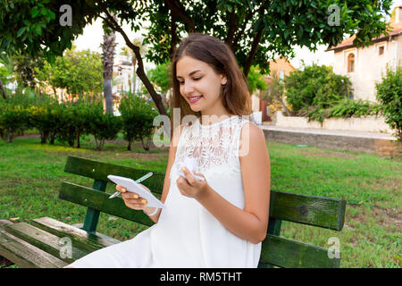 Ragazza carina è in possesso di una penna e un blocco note e carta sgualcita seduta sul banco di lavoro esterno. Foto Stock