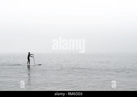 Goleta, CA, Stati Uniti d'America, 14 agosto 2016: A lone paddle boarder scivola attraverso la nebbia legato acque al largo del Refugio State Beach. Foto Stock