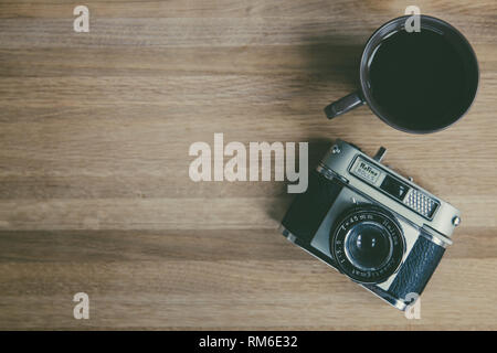 Guardando verso il basso a partire da sopra sulla scrivania in legno di un vecchio fotografo con vintage, 35mm Fotocamera e la tazza di caffè nero con spazio di copia Foto Stock