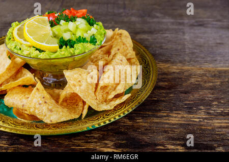 Guacamole con tortilla chips in ingredienti freschi su vintage rusty una ciotola di legno scuro dello sfondo. Vista da sopra con copia spazio. Foto Stock