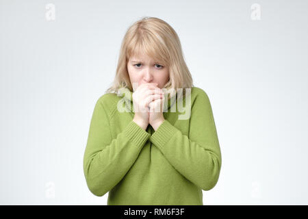 Congelamento di giovane donna in maglione verde cercando di ottenere il caldo. Foto Stock