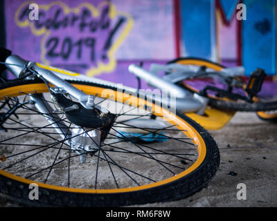 Vecchio rottame giallo biciclette sotto il cemento le scale con viola sullo sfondo di graffiti e anno nuovo tag per un colorato 2019 Foto Stock