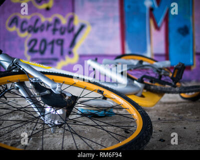 Vecchio rottame giallo biciclette sotto il cemento le scale con viola sullo sfondo di graffiti e anno nuovo tag per un colorato 2019 Foto Stock