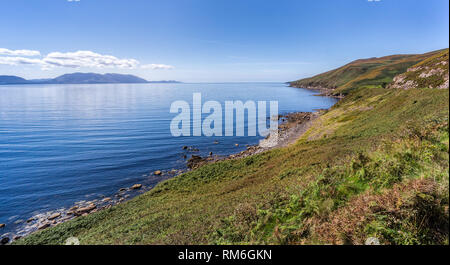 Cielo blu con il bianco puffy nuvole sulla rocciosa linea costiera e le montagne in distanza. Foto Stock