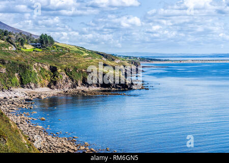 Cielo blu con il bianco puffy nuvole sulla rocciosa linea costiera e le montagne in distanza. Foto Stock