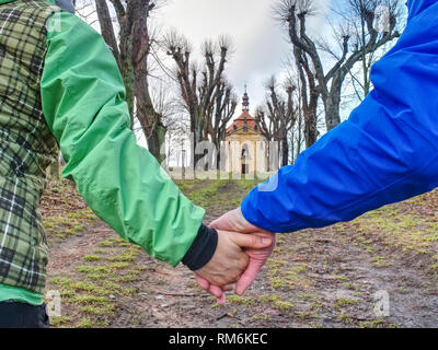 Giovane turista tenere mani e piedi attraverso un vicolo in parco, vecchia cappella alla fine Foto Stock