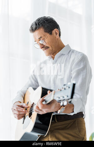 Uomo in pensione in bicchieri suonare la chitarra acustica a casa Foto Stock