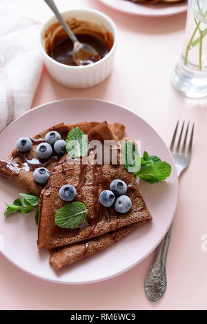Cioccolato artigianale crepes servita con mirtilli, il sugo di pomodoro e le foglie di menta su sfondo rosa. Messa a fuoco selettiva. Vista dall'alto. Spazio di copia Foto Stock
