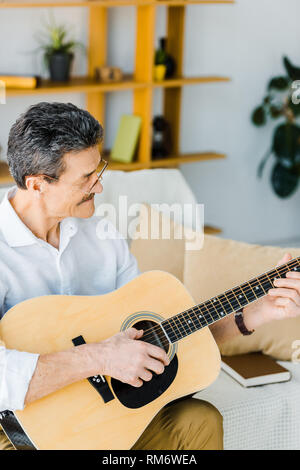 Allegro senior uomo suonare la chitarra acustica nel soggiorno Foto Stock
