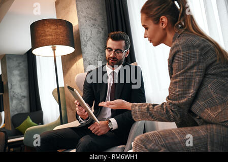 Guarda questa dashboard. Giovane imprenditore sorridente parlando con business donna e mostra al suo tablet mentre a cena in albergo costoso. Discutere i dettagli del contratto Foto Stock