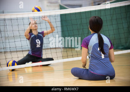 Lo sport per i disabili. La formazione. Due giovani donne sedute sul pavimento e giocando a pallavolo. Foto Stock