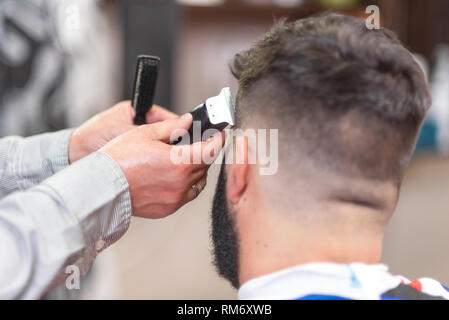 Bel uomo barbuto, getting taglio di capelli da un barbiere, con rifinitore elettrico in corrispondenza di Barberia . Foto Stock