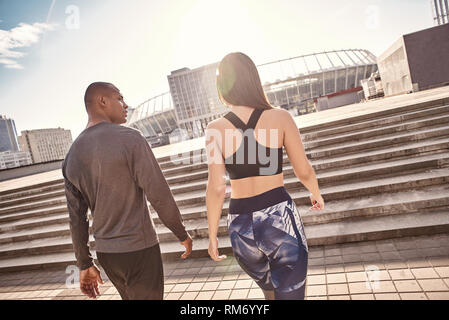 Dopo il fantastico allenamento. Vista posteriore della giovane coppia e multirazziale in abiti di fitness per andare a casa dopo la formazione attivo insieme. Ambiente urbano. Un sano giovane. Sport concetto di motivazione. Concetto di fitness. Donne bellezza. La vita sana. Esercitare insieme. Attività di mattina. Comune hobby Foto Stock