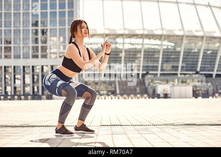 Squat perfetto. Sporty giovane donna in sport abbigliamento facendo squat durante l esercizio al di fuori del mattino. Sport concetto di motivazione. Concetto di fitness. Donne bellezza. Vita sana Foto Stock