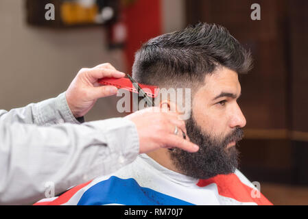 Bel uomo barbuto, avente pelo tagliato mediante forbici a Barber shop . Foto Stock