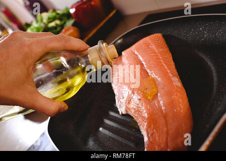 Materie filetto di salmone nella padella e cuocere versando olio d'oliva su di essa a cuocere. Foto Stock