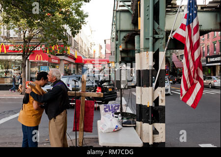 Street performer accoglie favorevolmente amico in un angolo di strada di Brooklyn a New York City, con bandiera americana appesa in pole Foto Stock