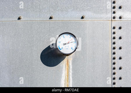 Un indicatore rotondo con un secco e rusty streak correndo giù al di sotto, è montata sulla parete di un acciaio zincato serbatoio acqua, con figure in blu su un quadrante bianco. Foto Stock