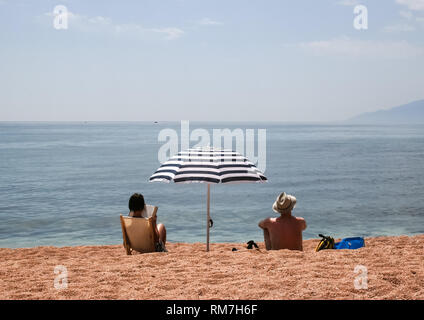 Persone sedersi ad un ombrello dal mare. Sedie e lettini da mare. Foto Stock