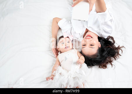 Una donna con un bambino facendo un selfie sdraiato sul pavimento in legno Foto Stock