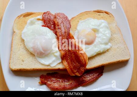 Le uova in camicia su toast bianchi con pancetta Foto Stock