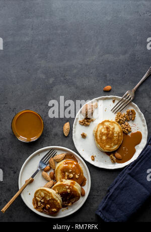 Festive blini con bolliti di latte condensato, due piastre bianche con forcella su sfondo grigio. Concetto di cibo festoso. Frittelle con Dolce caramello Foto Stock