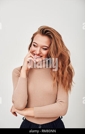 Ritratto di stupendo dolce signora con capelli biondi, indossando turtleneck beige, ella è ridere, cercando di distanza, in piedi isolato su sfondo bianco Foto Stock