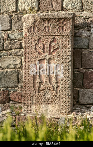 Un antico khachkar permanente al vecchio muro in un parco situato intorno al Monastero di Geghard situato nelle montagne di Armenia Foto Stock