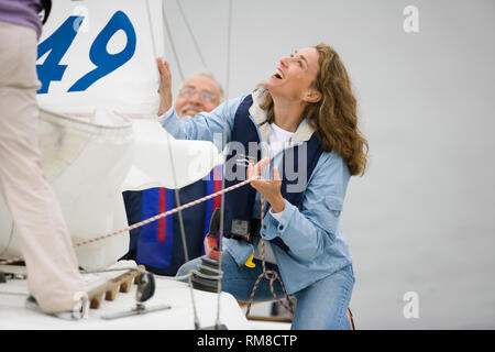 Coppia donna adulta abbassando la vela di una barca mentre suo marito guarda a. Foto Stock