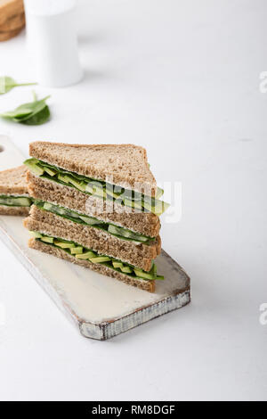 Vegano sani panini con verdure verdi e verdi. Avocado, spinaci e cetriolo brindisi sulla boardover taglio sfondo bianco. Impianto basato fo Foto Stock