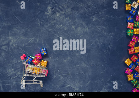 Piccolo carrello con presenta su sfondo nero. Carrello da un supermercato piena di colorati confezioni regalo. Shopping online concetto Venerdì nero un Foto Stock