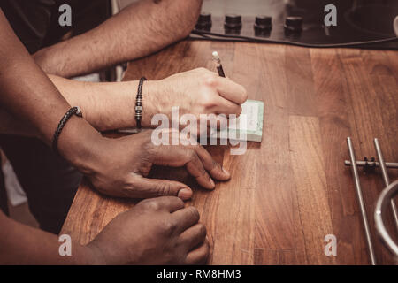 Un interracial gay giovane facendo una lista della spesa per i generi alimentari su una cucina in legno top a casa. Foto Stock