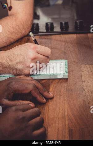 Un interracial gay giovane facendo una lista della spesa per i generi alimentari su una cucina in legno top a casa. Foto Stock