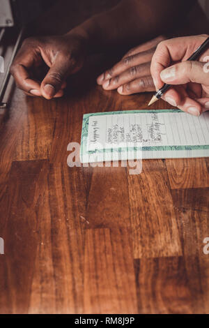 Un interracial gay giovane facendo una lista della spesa per i generi alimentari su una cucina in legno top a casa. Foto Stock