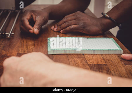 Un interracial gay giovane facendo una lista della spesa per i generi alimentari su una cucina in legno top a casa. Foto Stock