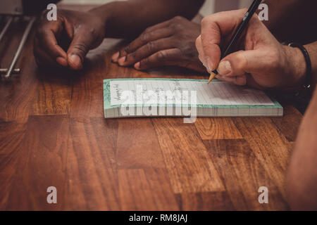 Un interracial gay giovane facendo una lista della spesa per i generi alimentari su una cucina in legno top a casa. Foto Stock