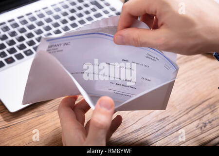 Vista in alzata di mano la rimozione di stipendio dalla busta sulla scrivania in legno Foto Stock