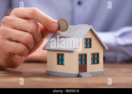 Close-up di una persona inserimento di moneta in casa Piggybank Foto Stock