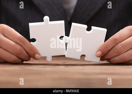 Close-up di commercianti la mano cercando di unire i due White Jigsaw Puzzle Foto Stock